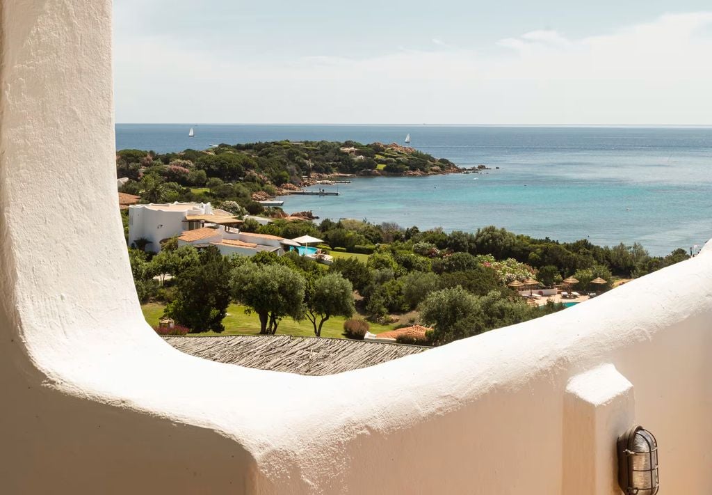 Elegant Mediterranean hotel room with panoramic sea views, white-washed walls, blue accents, and a private furnished balcony