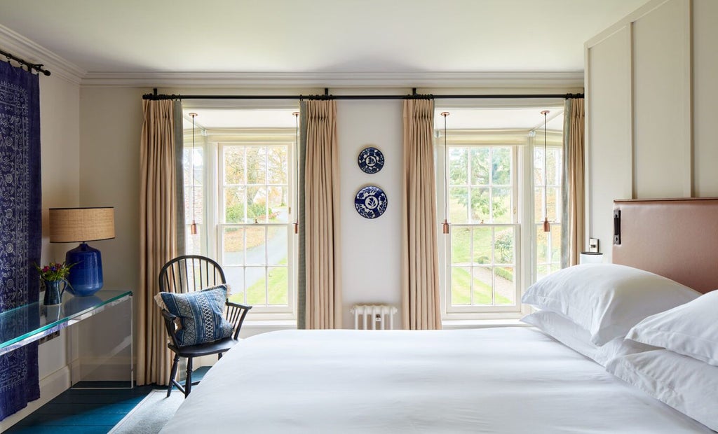 Elegant king bedroom with soft cream walls, plush white linens, antique wooden furniture, and soft natural light in luxurious Welsh countryside hotel room