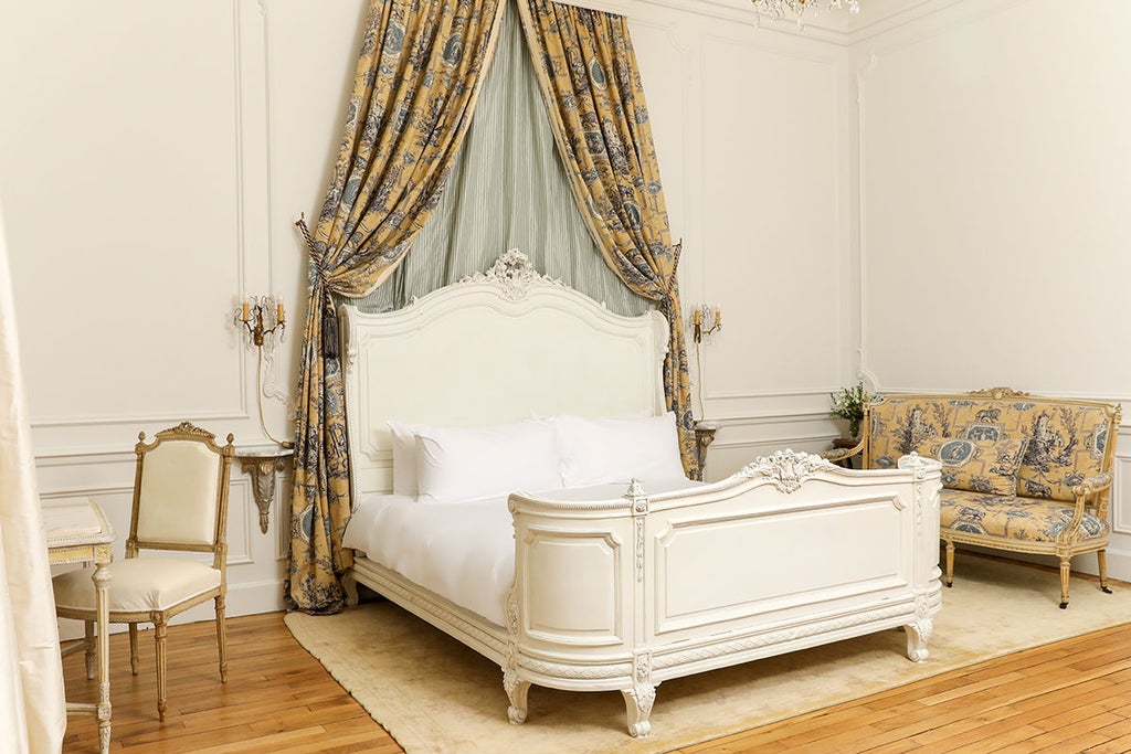 Elegant king room with period furnishings, ornate gold mirrors, silk drapes and garden views at historic French château hotel