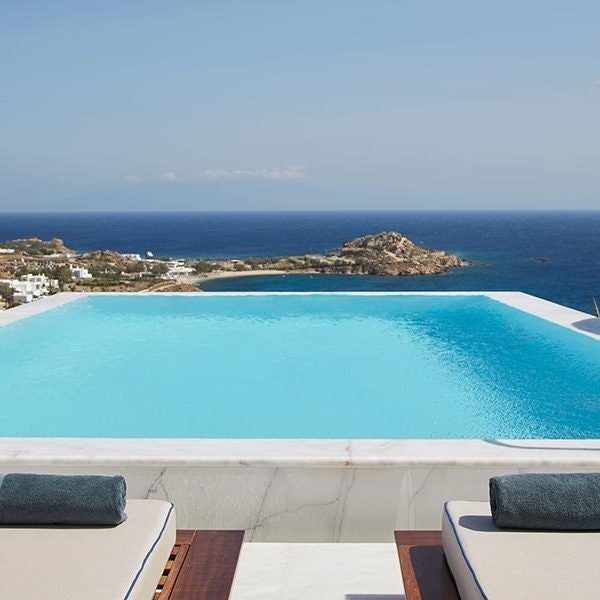 Luxurious white-walled suite with panoramic Aegean Sea view, minimalist design, private infinity pool, and sleek modern furnishings at Myconian Ambassador Hotel