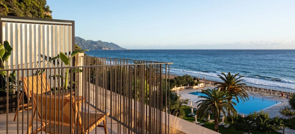 Elegant Patio Junior Suite with modern white decor, plush furnishings, and expansive sea view of Corfu's coastline through large glass sliding doors