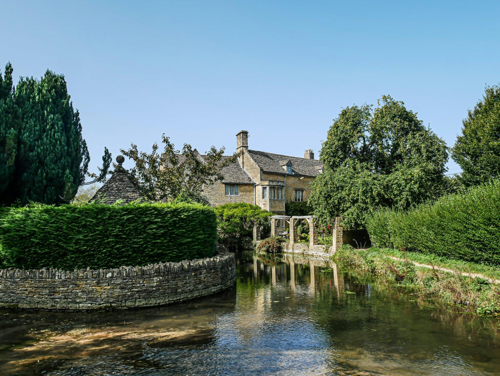 Rolling green hills dotted with honey-colored stone cottages and blooming wildflowers in the picturesque English Cotswolds countryside