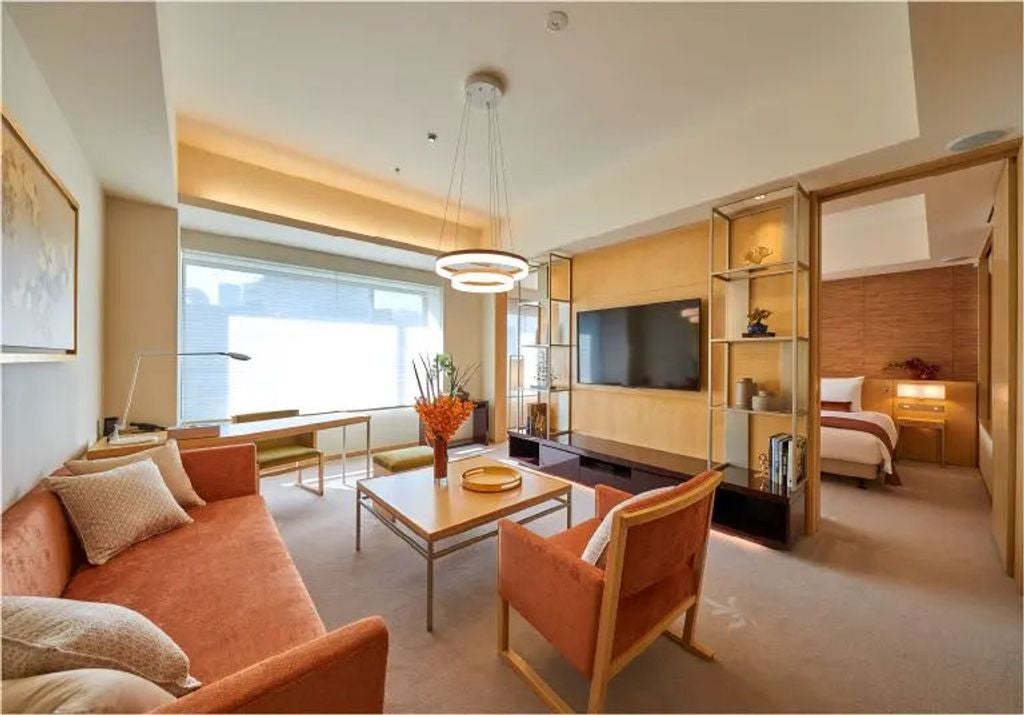 Elegant autumn-themed hotel suite with dark wood furnishings, red-gold accents, floor-to-ceiling windows, and city skyline views of Tokyo