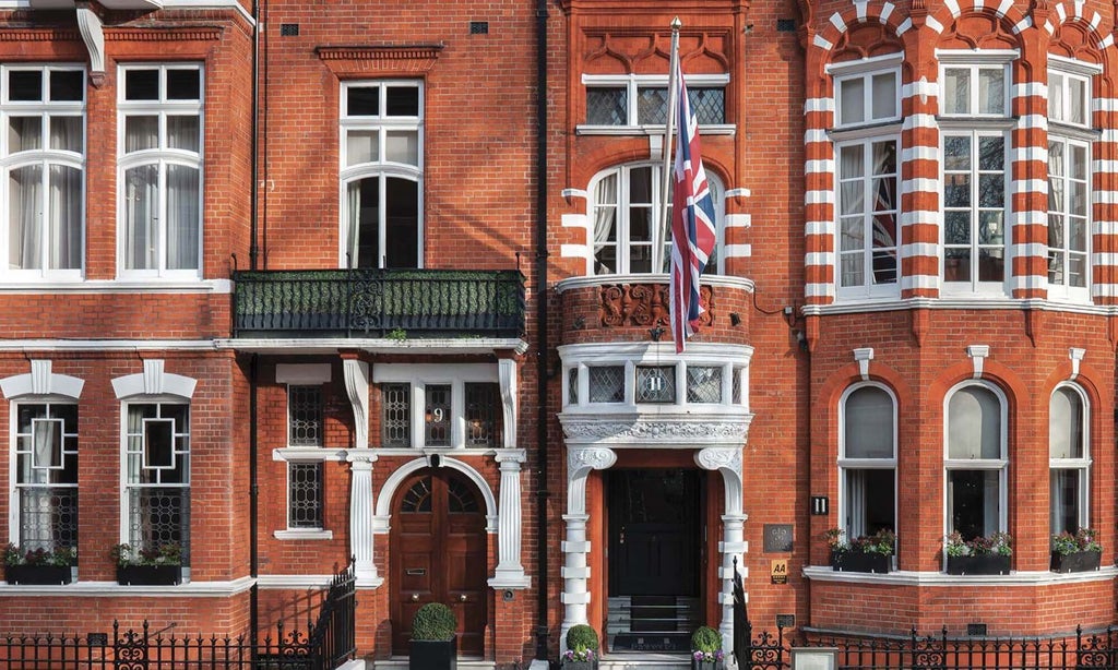 Victorian red-brick luxury hotel facade with ornate windows, wrought iron railings and classic lampposts along tree-lined Chelsea street