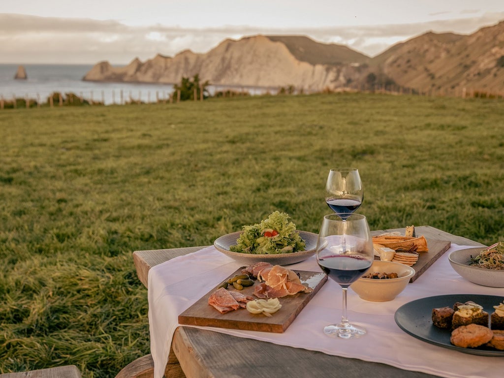 Luxurious clifftop lodge overlooking rolling hills and Pacific Ocean, featuring modern farmhouse architecture with stone and wood elements