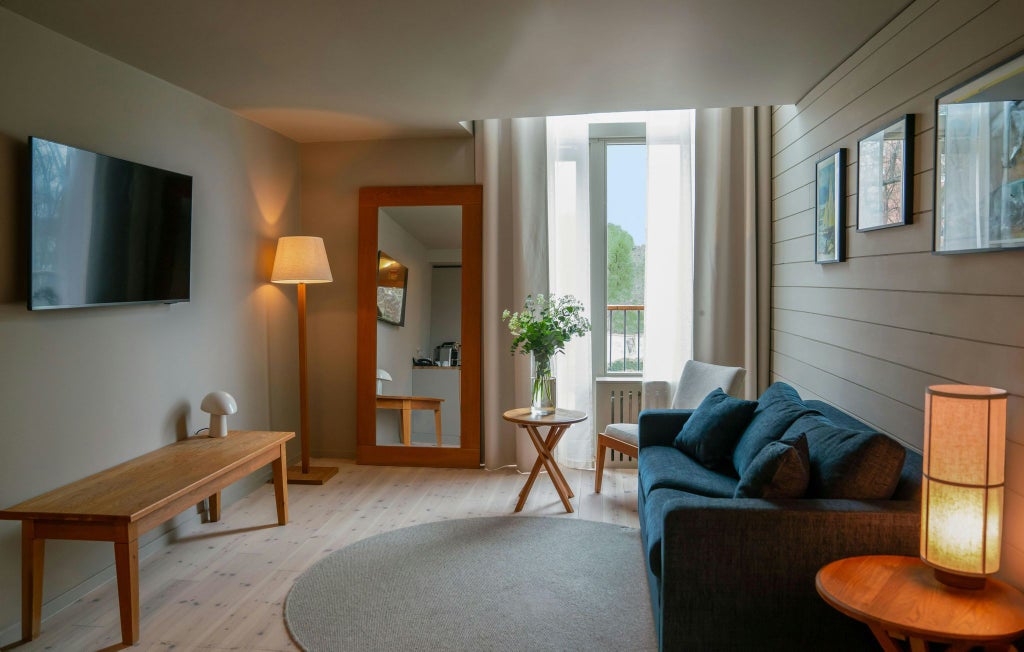 Elegant modern junior suite with panoramic windows, minimalist Nordic design, soft neutral tones, plush bedding, and sweeping view of Swedish landscape