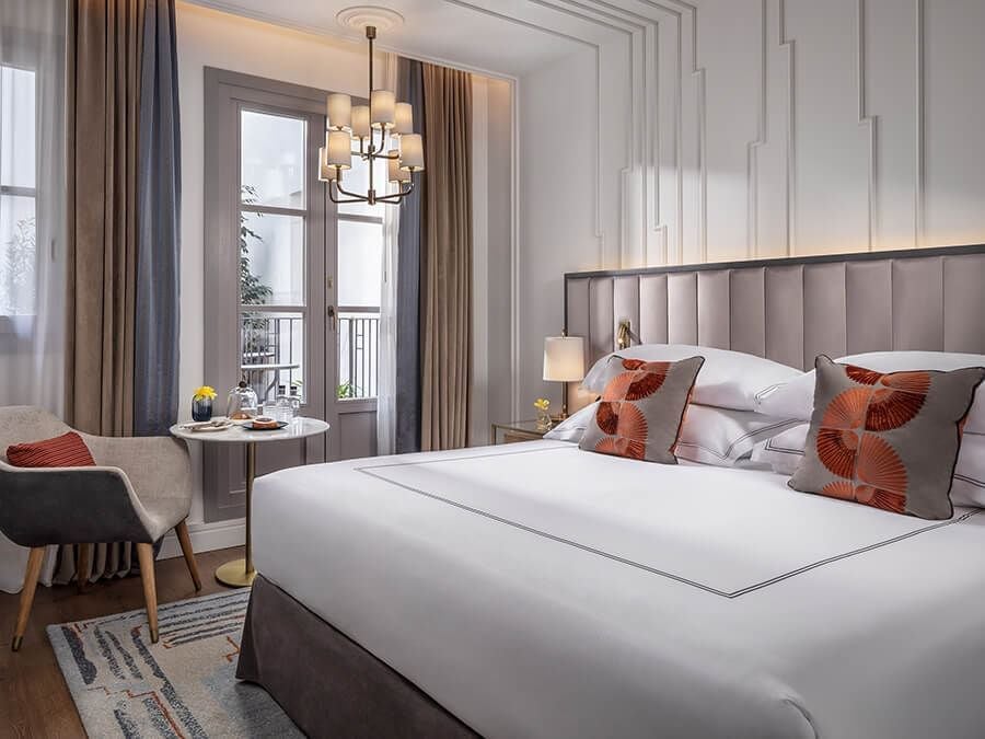 Elegant grand deluxe hotel room with classic Spanish design, plush white bedding, rich wooden furnishings, and refined traditional architectural details in warm tones