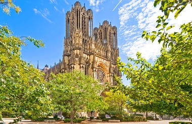 Gothic Reims Cathedral facade with intricate stone carvings, twin towers, and ornate rose window glowing in golden evening light