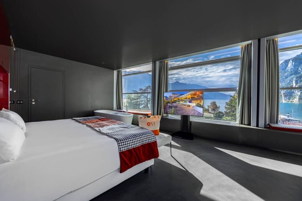 Opulent Italian hotel suite with panoramic lake view, marble floors, contemporary king-sized bed, and expansive floor-to-ceiling windows overlooking scenic landscape