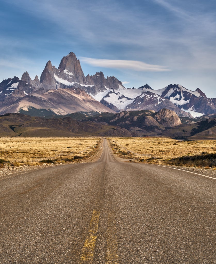 El Chalten village nestled beneath towering Mount Fitz Roy peaks, dramatic snow-capped mountains rising above colorful autumn forests