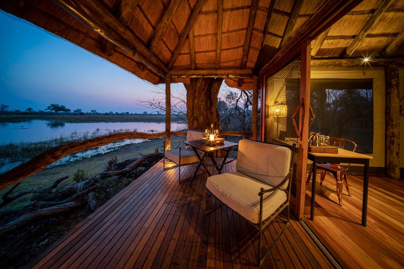 Elevated luxury safari tent overlooking Savuti Channel with private deck, canvas walls, and wooden flooring amid African bush