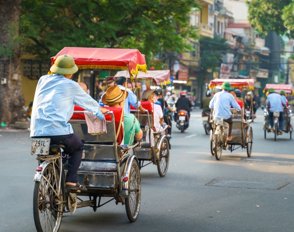 Vibrant street scene in Hanoi's Old Quarter, showcasing ornate colonial architecture, bustling markets, and traditional Vietnamese street life with lush greenery.