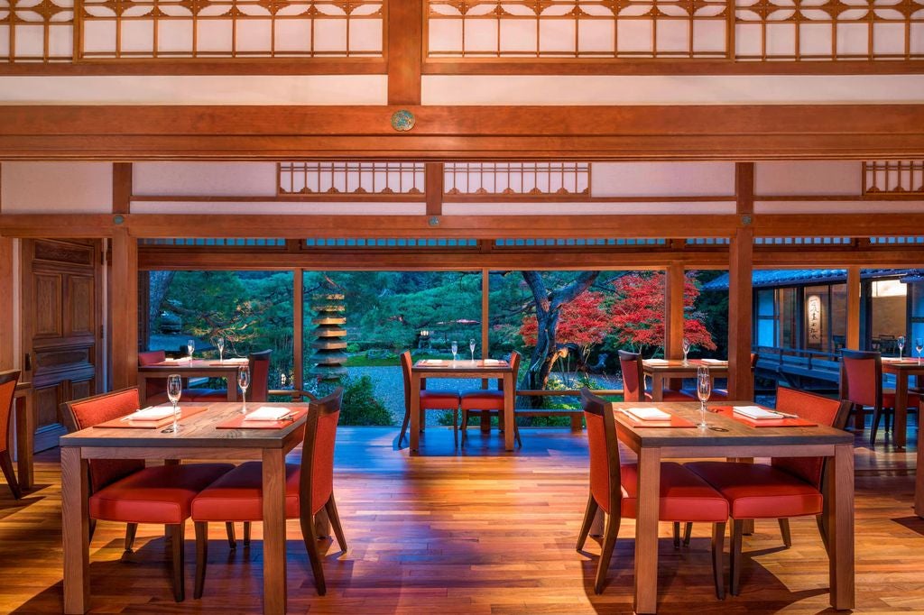 Traditional Japanese Ryokan hotel with wooden pavilion overlooking serene garden, featuring stone lanterns and cherry blossoms in bloom