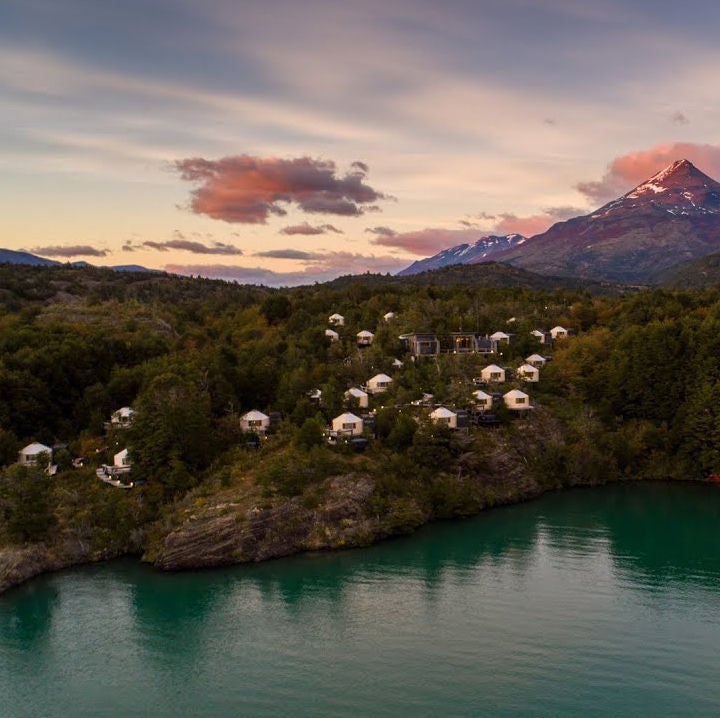 Modern luxury yurt cabin with geodesic dome roof nestled in Patagonian forest, featuring panoramic windows and wooden deck overlooking mountains