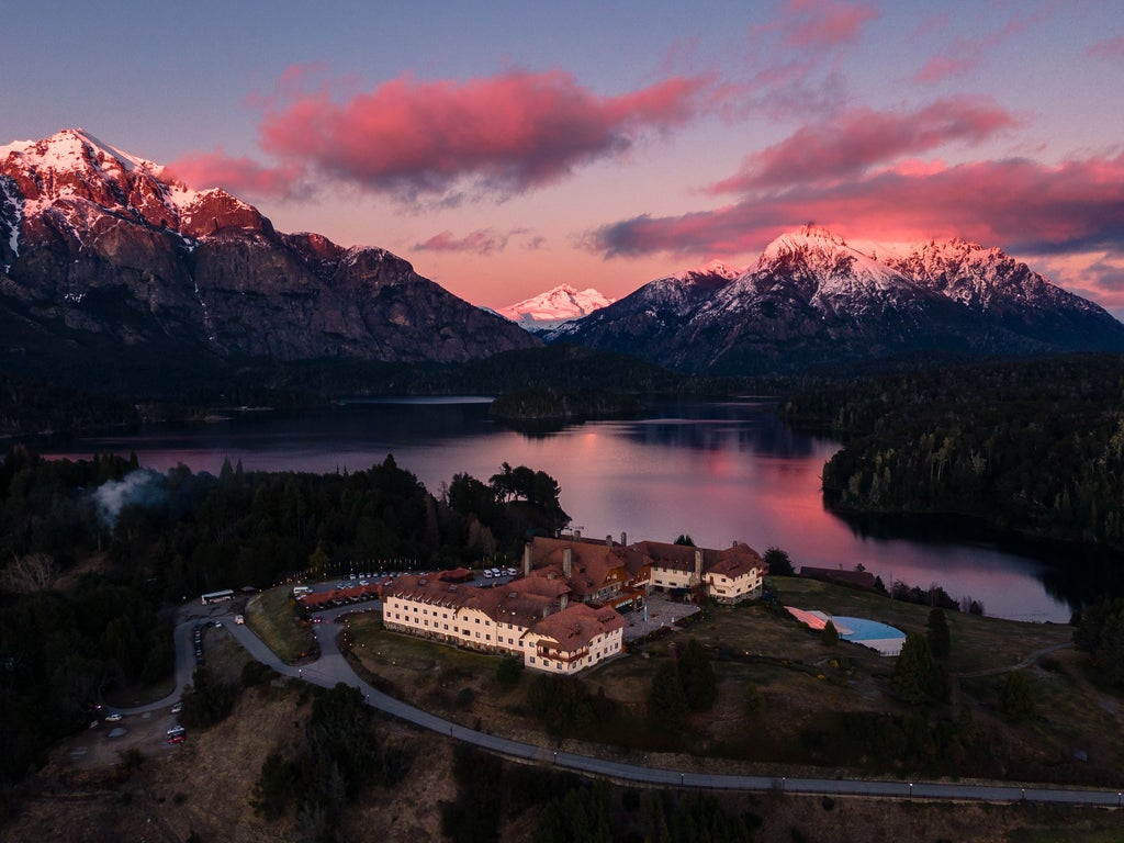 Majestic luxury resort nestled in Patagonian mountains, featuring alpine-style architecture with green roofs and surrounded by lake views