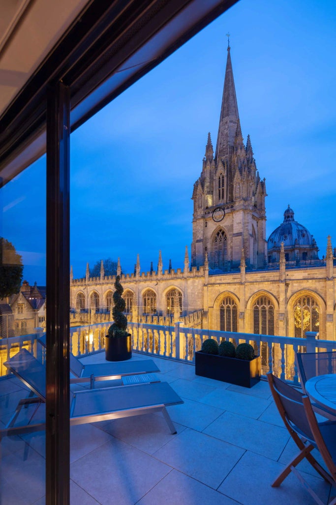 Elegant historic hotel room with large windows overlooking urban landscape, featuring vintage furnishings and refined British architectural details in soft neutral tones