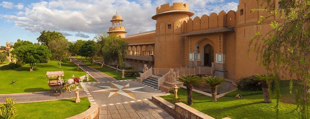 Luxurious Oberoi Rajvilas hotel featuring traditional Rajasthani architecture, ornate domes, and manicured gardens with a tranquil fountain.