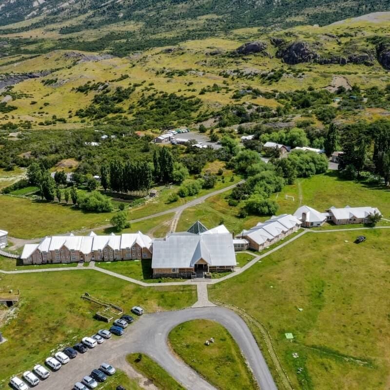 Luxurious eco-lodge nestled in rugged Chilean Patagonian landscape, with snow-capped mountains, wooden architecture, and pristine wilderness surrounding the hotel.