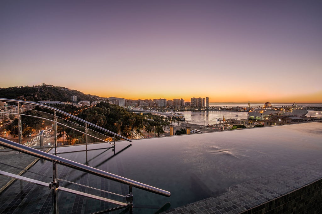 Modern luxury hotel facade with white balconies and Mediterranean-style architecture, situated in historic Malaga's city center at dusk