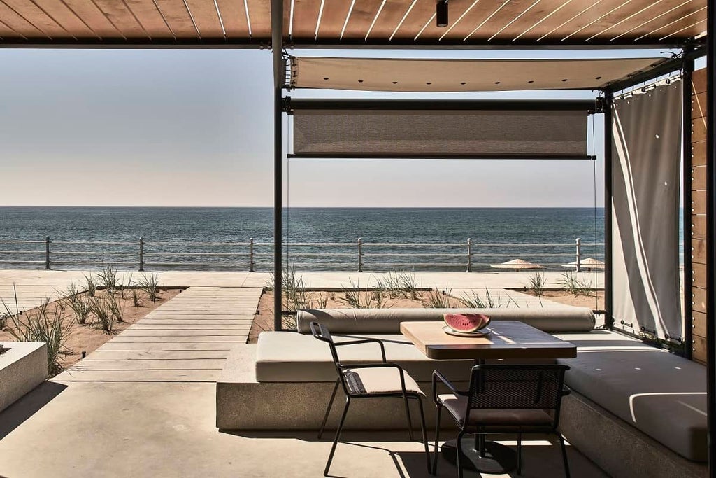 Minimalist coastal Greece hotel suite converted from wine tanks, featuring concrete walls, large windows, and panoramic Aegean Sea view at sunset