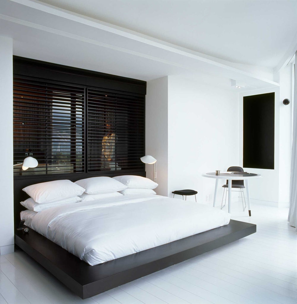 Modern, minimalist junior suite with clean white decor, sleek furniture, and floor-to-ceiling windows overlooking urban scenset landscape in Monterrey, Mexico.