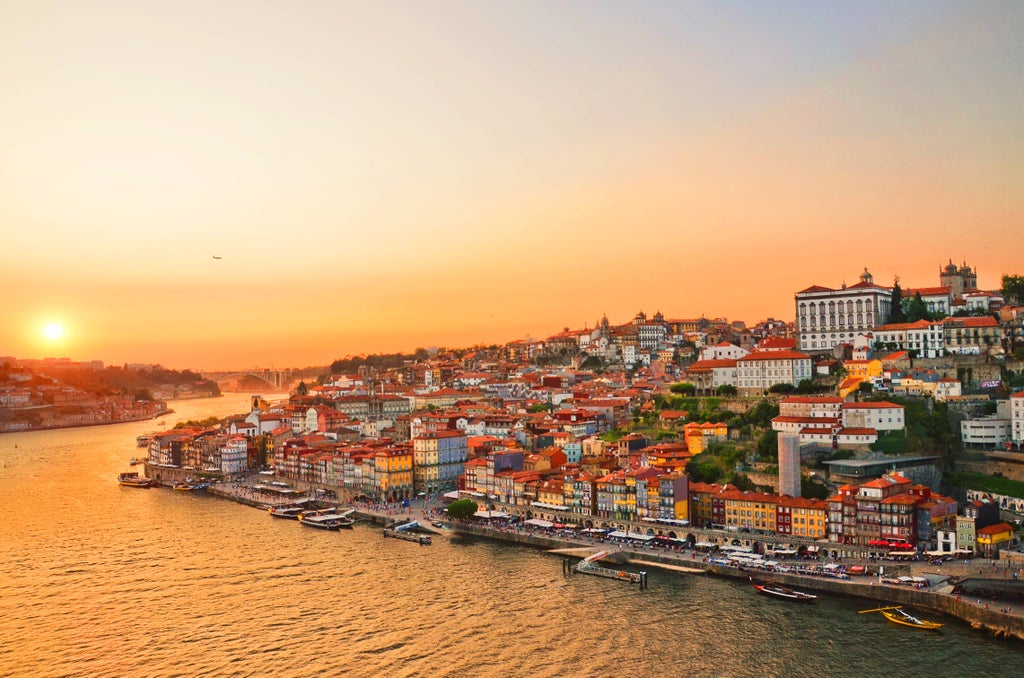 Golden sunlight illuminates a traditional wooden rabelo boat gliding on the calm Douro River with Porto's historic wine cellars lining the shore