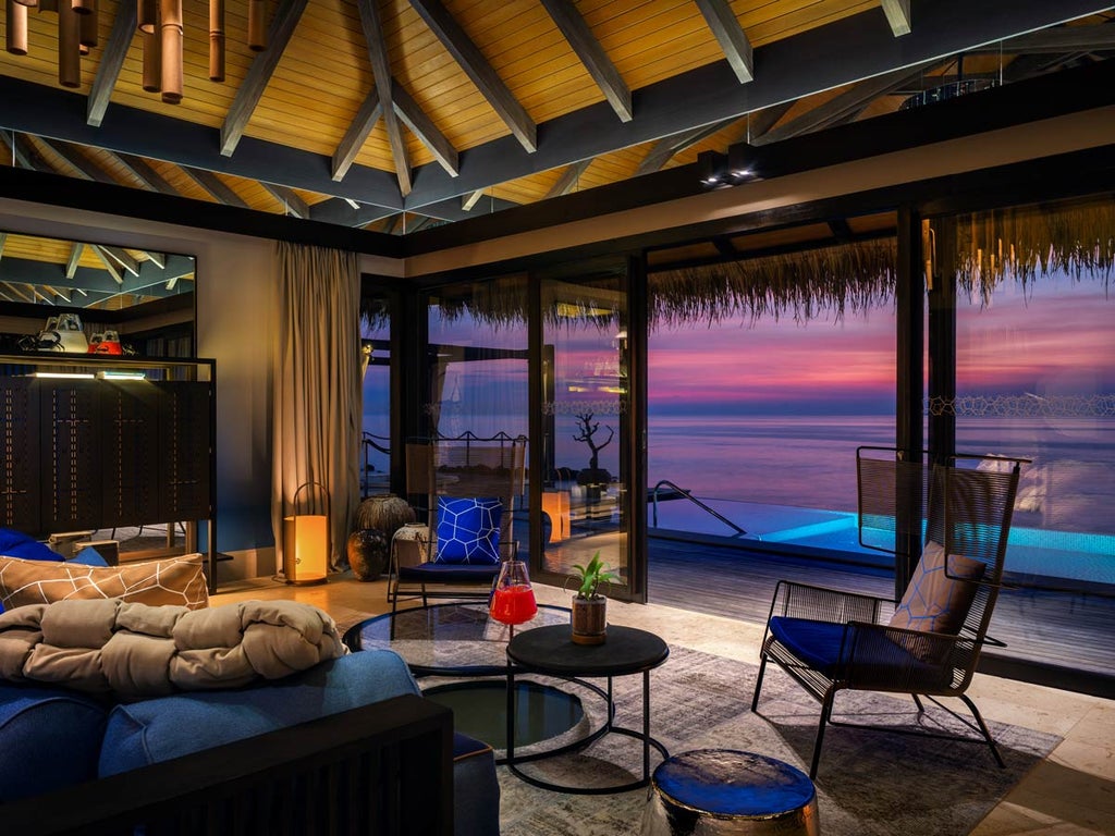 Overwater luxury villa with infinity pool extending over turquoise Maldivian lagoon, surrounded by palm trees and coral reefs