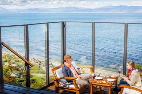 Luxurious beachfront resort nestled in Patagonian landscape, with rustic wood exterior, snow-capped mountain backdrop, and expansive glass windows overlooking coastal scenery