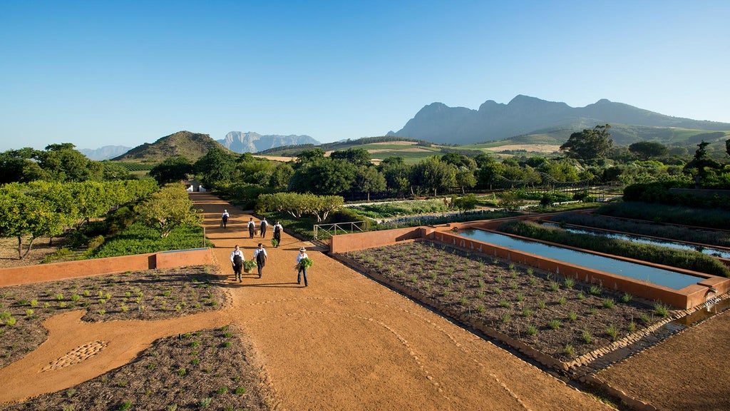 Elegant stone-walled suite with floor-to-ceiling windows overlooking manicured gardens and Cape Dutch architecture at South African wine estate