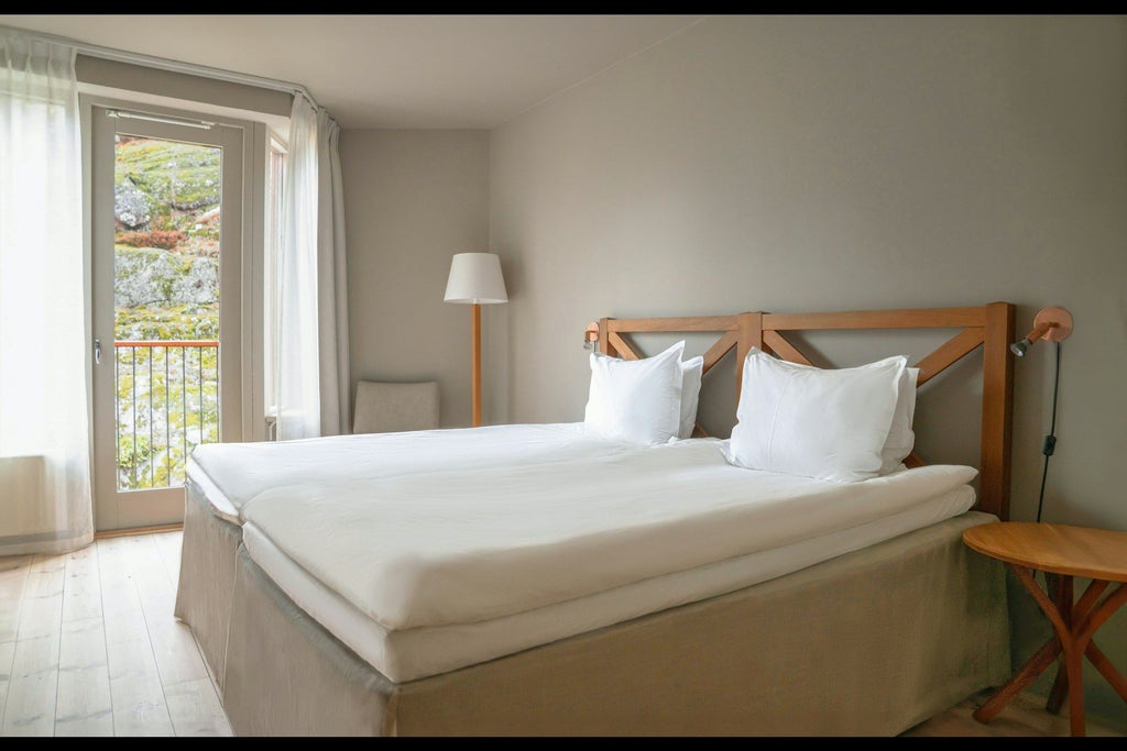 Minimalist Scandinavian hotel room with clean white linens, wooden floors, modern grey headboard, and large window offering natural light and scenic view