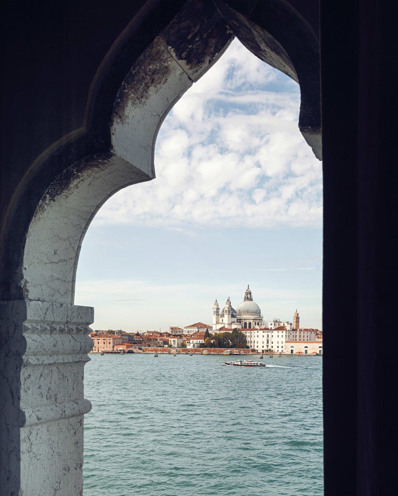 Elegant waterfront luxury hotel with terracotta walls and traditional Venetian architecture overlooking a marina filled with yachts at sunset