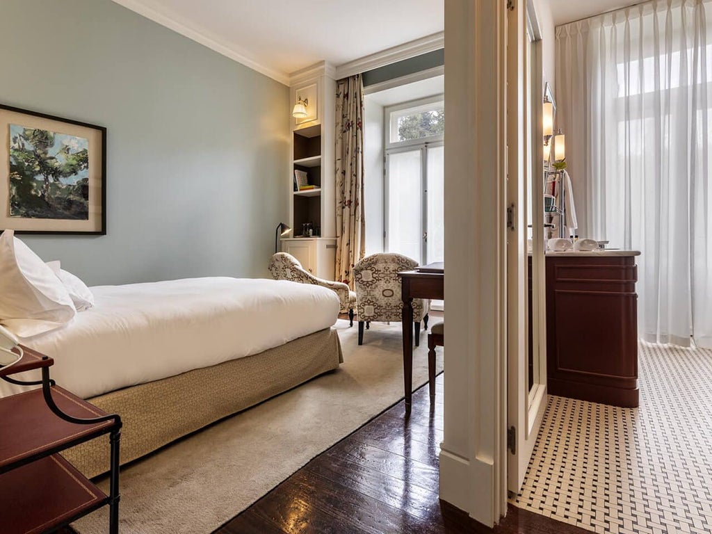 Elegant classic bedroom at Vidago Palace Hotel with ornate chandelier, plush white bedding, and opulent Portuguese marble bathroom details