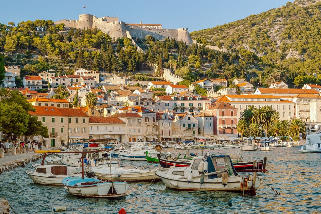 Two wooden boats moored in crystal-clear turquoise waters along Hvar's scenic coastline, with luxury villas perched on hillside