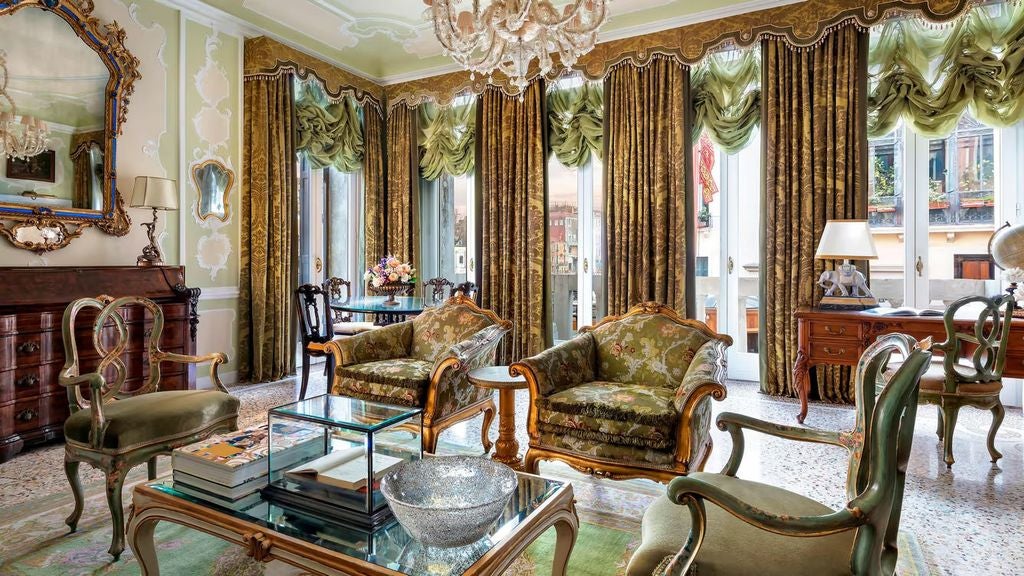 Opulent Italian presidential suite with ornate chandeliers, antique furnishings, and gold-framed artwork overlooking Venice's Grand Canal