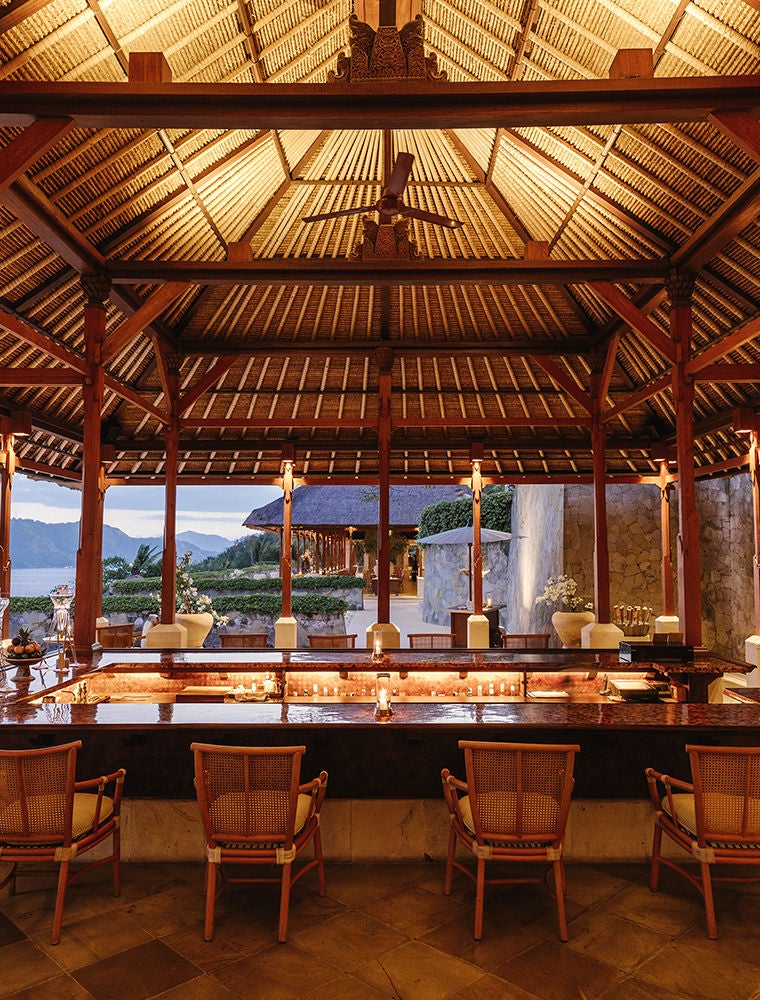 Three-tiered infinity pools cascade down a lush hillside, overlooking Bali's eastern coastline and the Lombok Strait at sunset