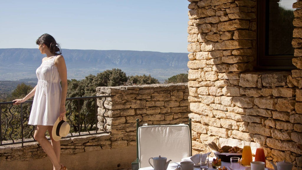 Elegant stone facade of Les Bories hotel in Provence, with manicured gardens, sun-lit terrace and infinity pool overlooking countryside