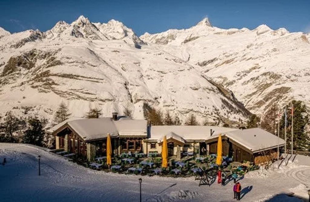 Luxurious mountain resort nestled in Swiss Alps, featuring stone and timber architecture, snow-covered balconies, and panoramic views