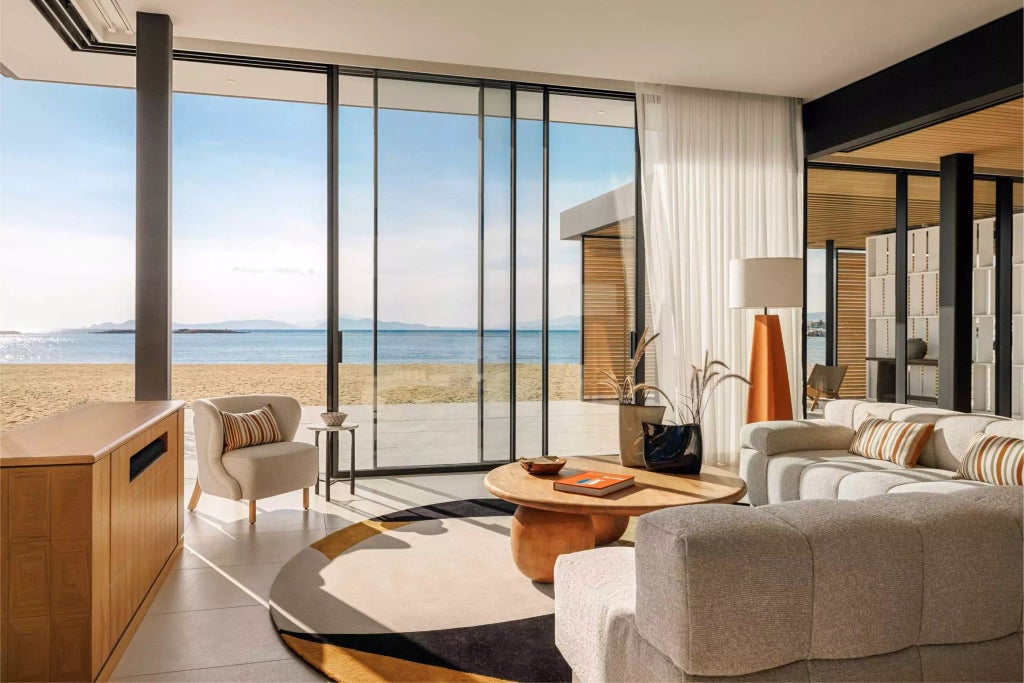 Luxurious two-bedroom topos suite with sweeping seafront views, elegant modern design, and expansive windows overlooking the scenic Greek coastline.