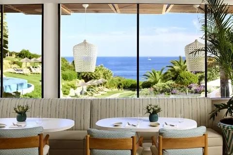 Luxurious coastal resort with infinity pool overlooking azure Atlantic waters, lush tropical gardens, and elegant Mediterranean-style architecture in the Algarve, Portugal