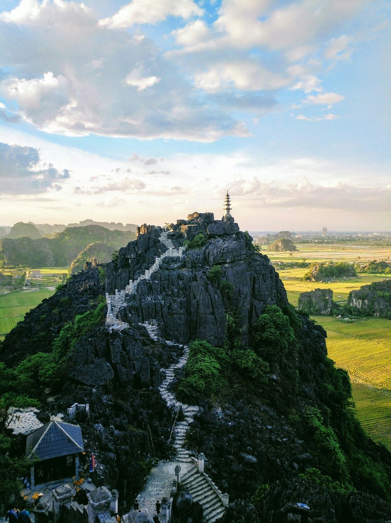 Scenic limestone karsts rising from emerald rice paddies, traditional wooden boat gliding through Trang An landscape, capturing Vietnam's serene natural beauty and cultural heritage.