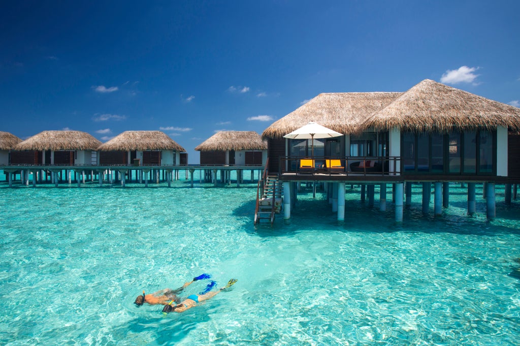 Overwater villas with thatched roofs extending into crystal-clear turquoise lagoon waters at Velassaru Maldives luxury resort