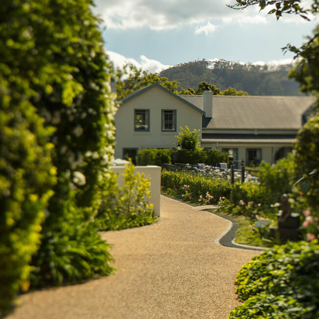 Art deco-style boutique hotel exterior in Franschhoek wine valley, with white colonial facade, manicured gardens and mountain backdrop