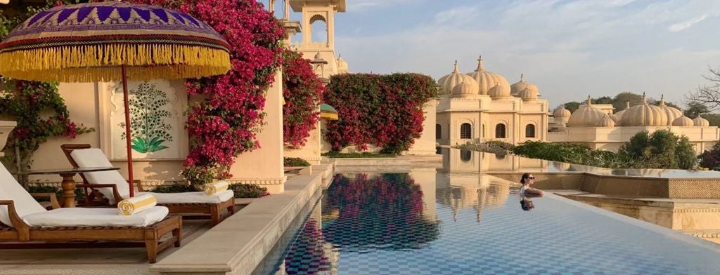 Ornate domed palace hotel with gold accents overlooking tranquil lake, featuring traditional Rajasthani architecture and manicured gardens