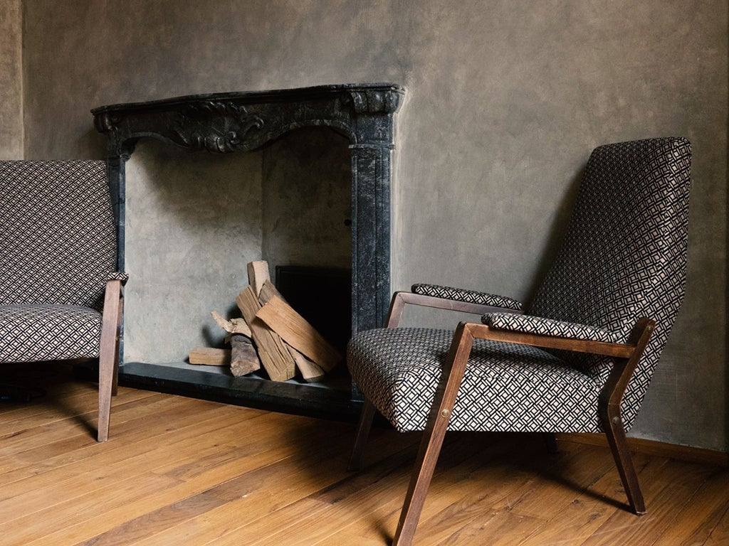 Elegant hotel suite with exposed stone walls, crystal chandelier, velvet armchairs, and vintage decor accents against natural light