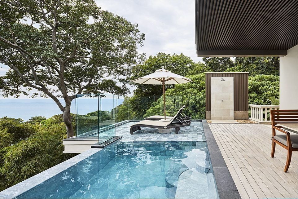 Luxurious infinity pool overlooking Andaman Sea at sunset, with modern loungers and tropical palm trees framing ocean views