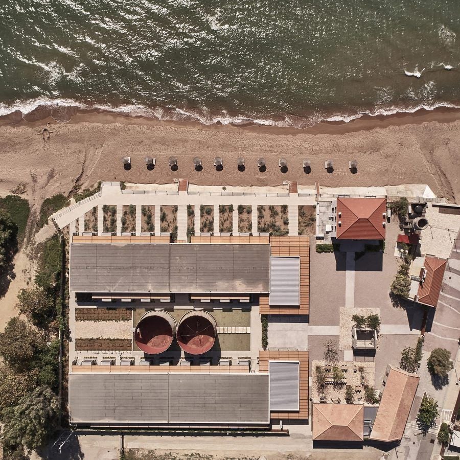 Luxurious minimalist beachfront hotel in coastal Greece, with sleek concrete structures nestled against azure Ionian Sea waters and sandy shoreline