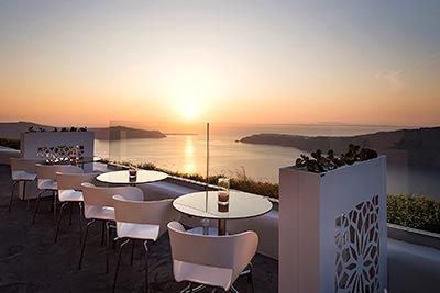 Luxurious seaside resort with white-washed Greek architecture, infinity pool overlooking azure Aegean waters, and lush Mediterranean landscape at sunset