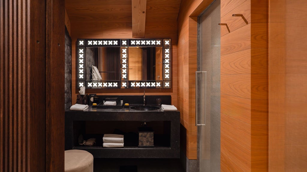 Luxurious alpine suite with minimalist Swiss design, dark wood paneling, floor-to-ceiling windows overlooking snow-capped mountain landscape at The Chedi Andermatt