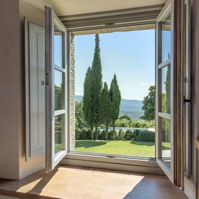 Elegant Tuscan hotel room with panoramic countryside view, soft natural light, wooden furnishings, and traditional Italian architectural details