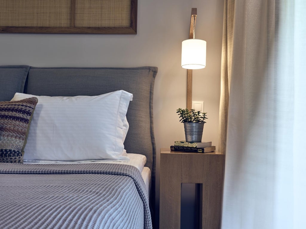 Spacious white villa bedroom with panoramic Aegean Sea view, elegant wooden furniture, minimalist design, and large glass doors opening to a private terrace